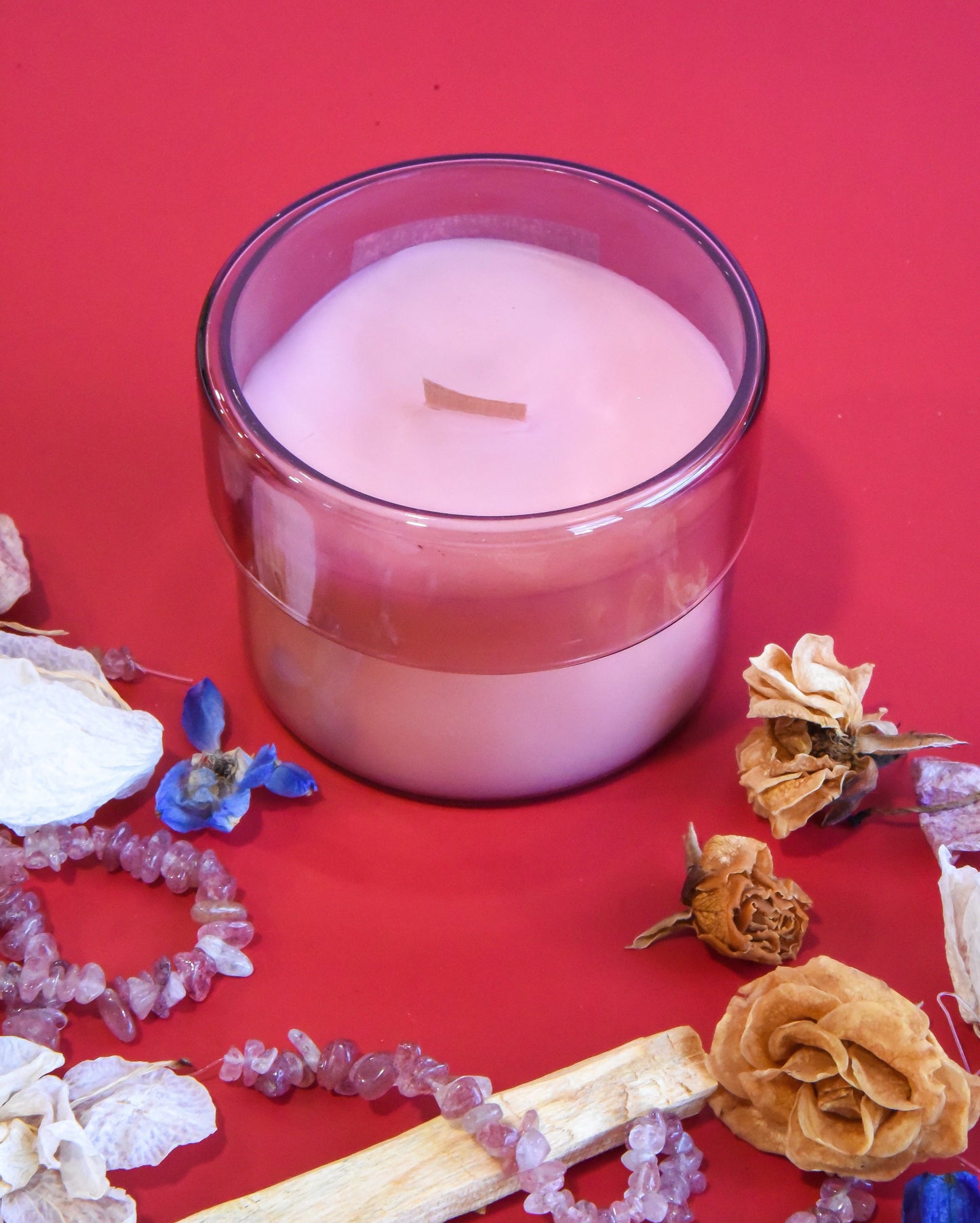 Translucent merlot glass wooden wick candle on a red surface with decorative elements.
